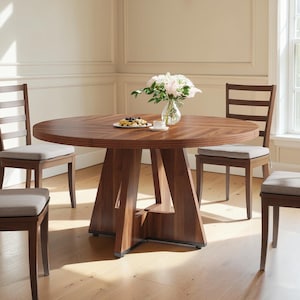May include: A round wooden dining table with a dark brown grain finish and a geometric pedestal base, accompanied by four wooden chairs featuring horizontal back slats and light gray upholstered seat cushions, topped with a glass vase of flowers.