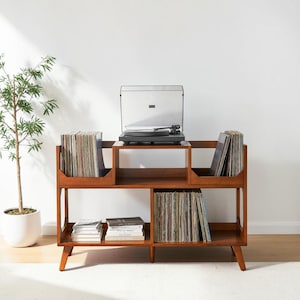 May include: A brown wooden media console with a rectangular frame and tapered legs. The unit features multiple open compartments for storing vinyl records and books, with a black turntable placed on the top center surface of the furniture.
