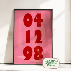 May include: A rectangular wall art print in a black frame featuring a bright pink background with the bold red numbers 04, 12, and 98 stacked in three rows. A small rectangular label in the corner displays the text CUSTOMISATION AVAILABLE ON REQUEST!