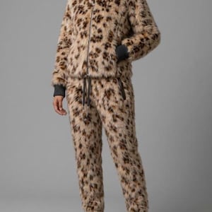 Puede incluir: Un conjunto de dos piezas compuesto por una chaqueta con cremallera y pantalones a juego, ambos hechos de piel sintética color canela con un estampado de leopardo marrón y negro. La chaqueta tiene cuello alto y puños acanalados gris oscuro.