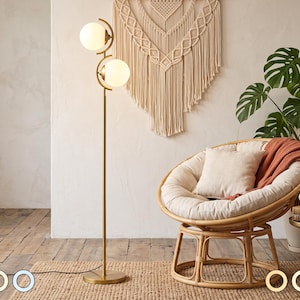May include: A tall floor lamp with a slender gold-toned metal stand and two spherical white glass shades. The lamp features a circular base and a vertical pole that supports the two lights, which are positioned at different heights and angles.