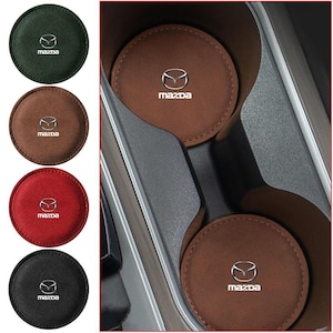 Può includere: Un set di sottobicchieri circolari per portabicchieri da auto in verde scuro, marrone, rosso e nero. Ogni sottobicchiere presenta una superficie testurizzata con il logo e la scritta Mazda stampati in bianco al centro. Sono mostrati singolarmente.