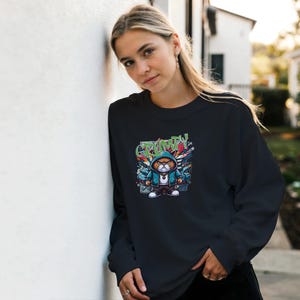 Könnte beinhalten: Ein schwarzes Langarm-Sweatshirt mit einem Grafikdruck einer orangefarbenen Katze, die einen blauen Kapuzenpullover und eine silberne Kette trägt. Die Katze hat einen strengen Gesichtsausdruck und ist von Graffiti-Elementen und dem Wort GRUMPY in Grün umgeben.