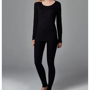May include: A solid black long-sleeve shirt with a rounded neckline paired with matching solid black leggings. The set features a simple, form-fitting design with long sleeves and full-length pants, providing a uniform appearance in a deep black color.