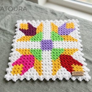 Puede incluir: Un lif de ganchillo hecho a mano de forma cuadrada con un patrón floral geométrico en hilo blanco, amarillo, verde, morado, rosa y rojo. La pieza tiene una construcción de puntos anudados texturizados e incluye una etiqueta de madera anatoura.
