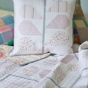 Pu&ograve; includere: Un copriletto bianco trapuntato con un motivo geometrico in tonalit&agrave; rosa e grigio. Il copriletto &egrave; ripiegato per rivelare un tessuto con motivo floreale sottostante. Due cuscini con motivi geometrici sono sul letto.
