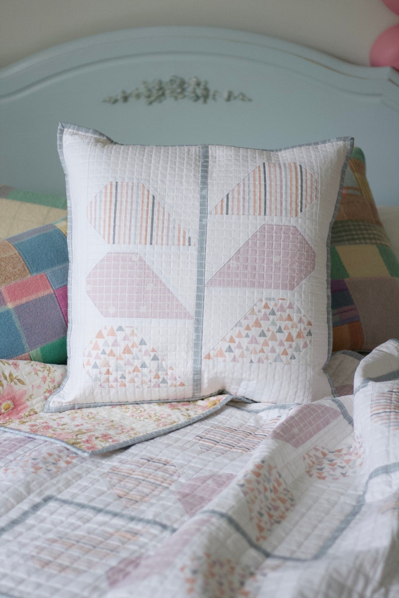 Pu&ograve; includere: Un copriletto bianco trapuntato con un motivo geometrico rosa e grigio. Un cuscino bianco con un motivo geometrico rosa e grigio &egrave; sul letto.