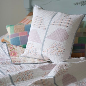 Pu&ograve; includere: Un copriletto bianco trapuntato con un motivo geometrico in tonalit&agrave; rosa e grigio. Il copriletto &egrave; decorato con diversi cuscini, tra cui un grande cuscino bianco con un motivo geometrico rosa e grigio.