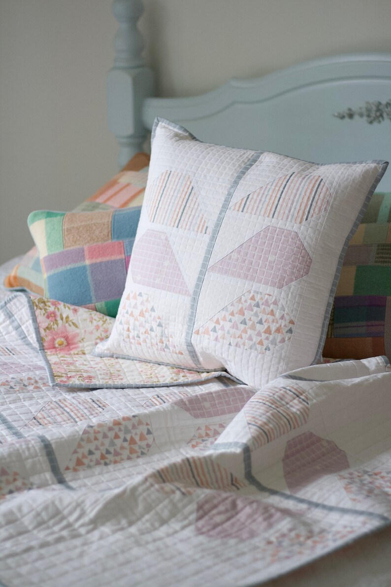 Pu&ograve; includere: Un copriletto bianco trapuntato con un motivo geometrico in tonalit&agrave; rosa e grigio. Il copriletto &egrave; decorato con diversi cuscini, tra cui un grande cuscino bianco con un motivo geometrico rosa e grigio.