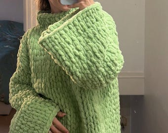 May include: A lime green chunky knit jumper featuring a high mock neck collar and long, wide sleeves. The garment is crafted from thick, soft yarn with a prominent textured stitch pattern, providing a voluminous and cosy appearance.