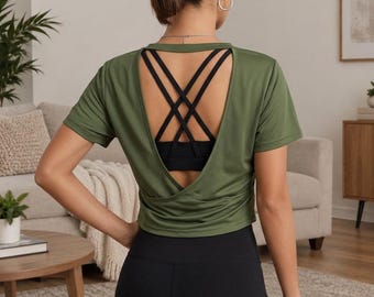 May include: An olive green short-sleeved athletic top featuring an open back design with a crisscross strap detail. The shirt is layered over a black sports bra and paired with black leggings, showcasing a functional and breathable activewear style.