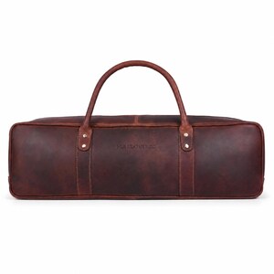 Pode incluir: Uma mala de viagem retangular em couro castanho escuro com uma única alça arqueada. A mala apresenta costuras visíveis, rebites na cor latão nas fixações da alça e o texto HLB LEATHER CO. gravado no centro do painel frontal.