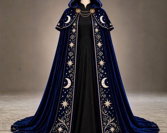 May include: A floor-length royal blue velvet hooded cloak featuring gold embroidered celestial motifs including crescent moons and stars along the front edges. The cloak is secured at the neck with a gold chain and circular clasps over a black dress.