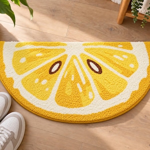 Peut inclure: Un tapis de bain semi-circulaire arborant un motif de tranche de citron jaune et blanc. Ce tapis texturé présente un design d'agrume détaillé avec des segments jaune vif, des bordures blanches et de petites graines brunes disposées en rayon.