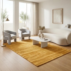 Könnte beinhalten: Ein rechteckiger senfgelber Teppich mit dezenter horizontaler Textur, der auf einem hellen Holzboden unter einem weißen, geschwungenen Sofa, zwei hellgrauen Sesseln und einem weißen, gesprenkelten Couchtisch mit einer skulpturalen Vase liegt.