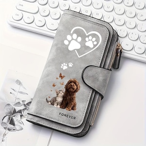 May include: A grey wallet featuring a white heart and paw print graphic at the top. Below, a brown dog and a grey tabby cat sit together surrounded by small butterflies. The word FOREVER is printed in black at the bottom of the wallet flap.