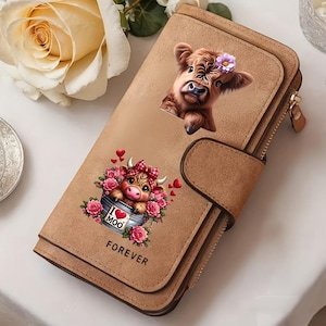Op de afbeelding: Een beige portemonnee met een afbeelding van een pluizige bruine koe met een paarse bloem op de kop, en een tweede afbeelding van een koe in een emmer omringd door roze rozen met de tekst I LOVE MOO en FOREVER in zwarte letters gedrukt.