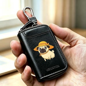 May include: A black leather key case with a zipper closure and a silver metal carabiner clip. The front features a graphic of a tan pug wearing a yellow sun hat. The word GEUSTOS is embossed in the bottom right corner of the black leather surface.