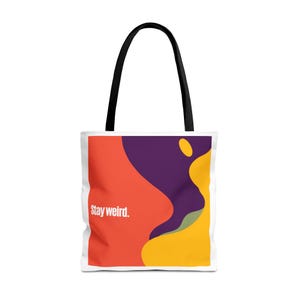 Könnte beinhalten: Eine weiße Tragetasche mit schwarzen Henkeln und einem grafischen Design aus abstrakten, wellenförmigen Formen in Rot, Lila und Gelb. Der Text "Stay weird." ist in Weiß auf der linken Seite der Tasche über dem roten Bereich des Designs gedruckt.