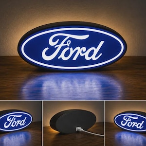 May include: An oval-shaped Ford logo sign featuring a deep blue background with white lettering and a glowing white border. The sign is illuminated from within and includes a black back panel with a white power cord attached to the center port.