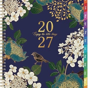 May include: A 2027 spiral-bound planner with a dark blue cover featuring white hydrangea clusters, teal and gold floral illustrations, and a small brown bird. The text "2027" and "Enjoy the little things" are printed in gold. Includes monthly side tabs.