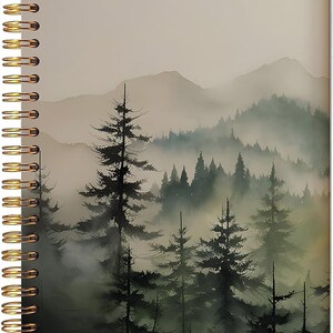 May include: A spiral-bound notebook featuring a cover illustration of a dense forest with tall evergreen trees shrouded in thick, misty fog. The background displays soft, muted layers of rolling mountains in shades of gray and green. The binding consists of a metallic gold-colored wire coil along the left edge.