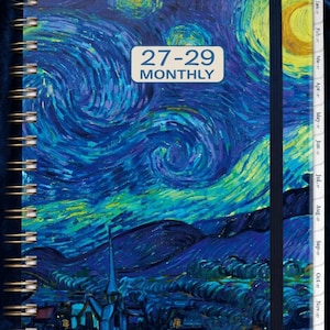May include: A spiral-bound monthly planner featuring a cover with a blue and yellow swirling night sky painting. The text 27-29 MONTHLY is printed in a white rectangular box. The planner includes side tabs labeled with months from Jan to Dec.