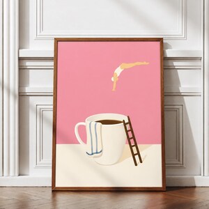 May include: A framed art print featuring a pink background with a person in a white swimsuit diving into a large white coffee mug filled with dark liquid. A blue and white striped towel hangs over the rim, and a brown ladder leans against the mug.