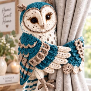 May include: A crochet owl curtain tieback featuring teal and beige yarn. The owl has large dark eyes with long lashes, a cream-colored face with brown speckles, and wings that wrap around a light gray curtain to hold it in place securely.