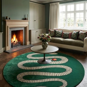May include: A large, circular, deep green area rug featuring a long, winding snake with a cream-coloured, grid-patterned body. The snake design curves across the rug's surface, incorporating a single red apple graphic near the centre.