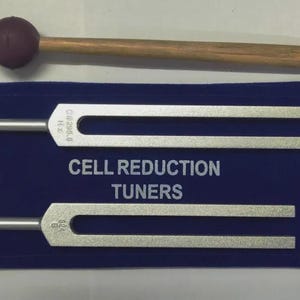 May include: Two silver-coloured metal tuning forks and a wooden mallet with a dark brown rubber head. The forks are labelled C 295.8 Hz and 824 Hz. The text CELL REDUCTION TUNERS is printed in white on a dark blue rectangular fabric pouch.
