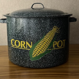 May include: A large, speckled black enamel corn pot with a matching lid. The pot features the words "CORN POT" in yellow, along with a graphic of an ear of corn. It has two side handles and a handle on the lid.