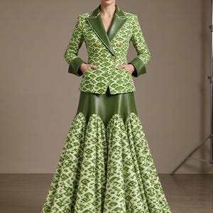 Puede incluir: Un conjunto de blazer de doble botonadura y falda larga con un patrón geométrico en verde y blanco. La blazer tiene solapas y puños en verde sólido con botones dorados. La falda presenta un canesú verde sólido y un bajo acampanado.
