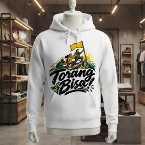 Puede incluir: Una sudadera con capucha blanca que presenta un estampado gráfico de tres excursionistas escalando un pico de montaña con una bandera amarilla. El texto Torang Bisa! está impreso en negro debajo de la ilustración. Tiene mangas largas.