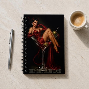 May include: A spiral-bound notebook featuring a black cover with a graphic illustration of a figure in a red dress sitting inside a large martini glass. The figure has small horns and a tail. The text SIP.SIN.REPEAT is printed at the bottom.