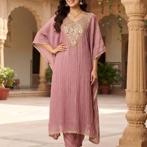 May include: A dusty rose kaftan-style tunic featuring a textured, crinkled fabric and a V-neckline adorned with intricate gold embroidery, sequins, and mirror work. The garment has wide, flowing sleeves and a matching pair of straight-leg trousers.
