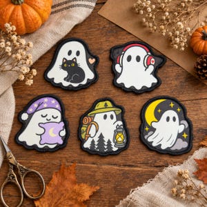 Puede incluir: Cinco parches bordados con fantasmas blancos: uno con un gato negro, uno con auriculares rojos, uno con gorro de dormir morado y almohada, uno de excursión con mochila y linterna, y uno flotando cerca de una luna creciente amarilla.