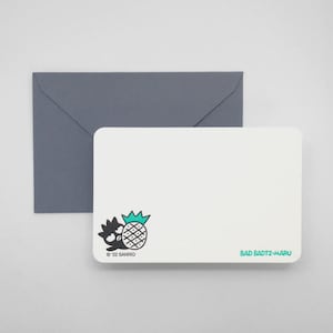 May include: A white stationery card with a cartoon pineapple and character illustration, accompanied by a gray envelope. The card features the text "BAD BADTZ-MARU" and "© 22 SANRIO".