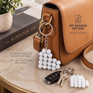 May include: A DIY white beaded heart pattern keychain with a silver metal ring and chain. The text reads PDF BEADING PATTERN INSTANT DOWNLOAD and DIY WHITE BEADED HEART PATTERN PDF INSTRUCTIONS INCLUDED. A tan leather bag and keys are visible.