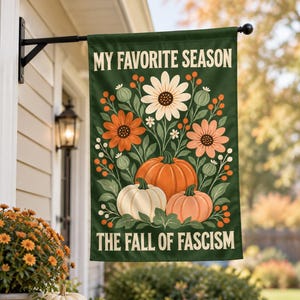 Może przedstawiać: Prostokątna ciemnozielona flaga ogrodowa z napisem MY FAVORITE SEASON na górze i THE FALL OF FASCISM na dole. W centrum znajduje się botaniczna ilustracja przedstawiająca białe i pomarańczowe kwiaty, zielone liście oraz trzy dynie.
