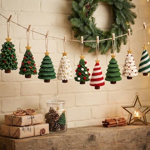 May include: A garland of nine crocheted Christmas tree ornaments hanging from a string with wooden clips. Each tree features a small gold star at the top and a brown trunk. The designs include solid green, white, and red-and-white striped patterns.