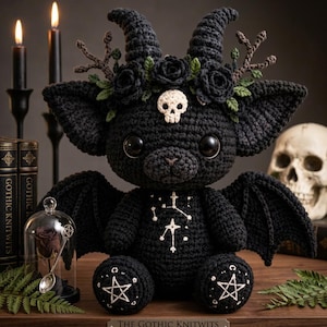 May include: A black crocheted plush creature with large dark eyes, curved horns, and bat-like wings. It features a white skull on its forehead, a crown of black roses with green leaves, and white embroidered star patterns on its chest and feet.