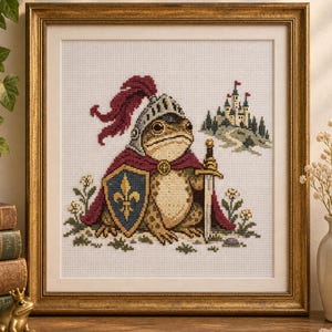 May include: A cross-stitch embroidery in a gold frame depicting a frog wearing a silver knight helmet with a red plume and a maroon cape. The frog holds a sword and stands beside a blue shield with a gold fleur-de-lis, with a castle in the background.