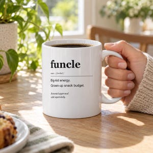 May include: A white ceramic mug featuring black printed text that defines the word funcle as having big-kid energy and a grown-up snack budget, with the additional note that parental approval is sold separately. The mug contains dark liquid.