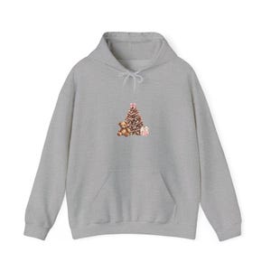 Può includere: Una felpa con cappuccio grigio melange caratterizzata da una grafica centrale con un albero di Natale decorato, un orsacchiotto marrone seduto alla base e un piccolo pacchetto regalo rosa. La felpa include una tasca a marsupio e lacci.