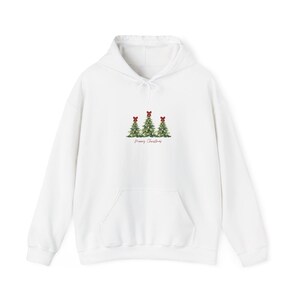 Può includere: Una felpa con cappuccio bianca caratterizzata da una grafica con tre alberi di Natale verdi in stile acquerello, ciascuno sormontato da un piccolo fiocco rosso. Sotto gli alberi, il testo Merry Christmas è stampato in corsivo rosso.