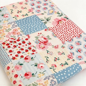 May include: A fabric quilt featuring a patchwork design of various squares. The patterns include floral prints with pink, red, and yellow flowers on cream, blue, and white backgrounds, alongside blue and white polka dots and red and white dots.