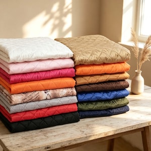 May include: A stack of folded quilted fabric squares in various colors including white, pink, magenta, orange, tan, brown, blue, olive green, and black. One square features a beige and brown patterned print. Each piece has a diamond stitch pattern.
