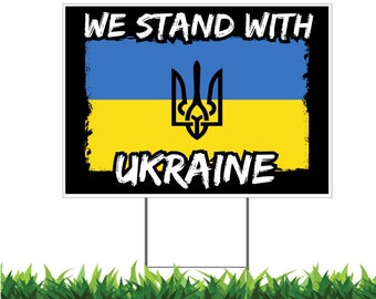 May include: A yard sign with the text "WE STAND WITH UKRAINE" in white, set against a blue and yellow background, representing the Ukrainian flag. The sign features a black border and a trident symbol.
