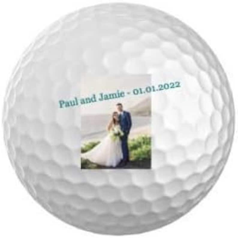 Puede incluir: Bola de golf blanca con un dise&ntilde;o personalizado que incluye una foto de una pareja de reci&eacute;n casados y el texto "Paul y Jamie - 01.01.2022".